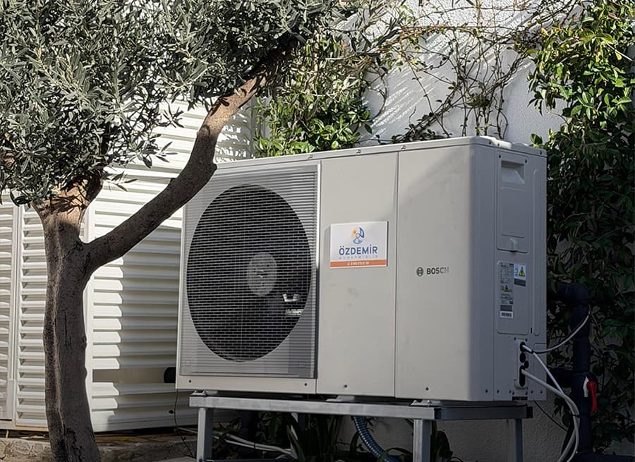 Villa bahçesinde zeytin ağacının altına yerleştirilmiş Bosch ısı pompası dış ünitesi